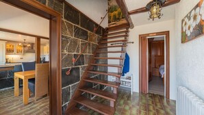 Eine Treppe mit Holzsitzen führt zu einer zweiten Etage, ein Küchenbereich mit Steinwand und ein Essbereich mit Holztisch und Stühlen.