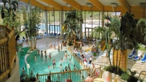 An indoor swimming pool with a central water slide, surrounded by lounge chairs and tables. - Ferienhaus in Willingen nahe Skipisten (Willingen)