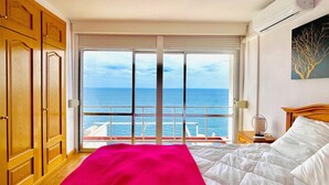 Un dormitorio con una cama grande, vista al mar, armarios de madera y una mesita de noche con lámpara.