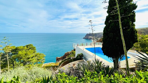 Vista costera con cielo despejado, piscina y acantilado.