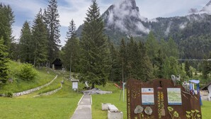 Una entrada a un parc natural amb un camí que condueix a una construcció de fusta, envoltada d'arbres i muntanyes.