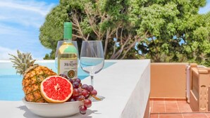 A table with a bottle of wine, a glass, a bowl of fruit, and a pineapple.