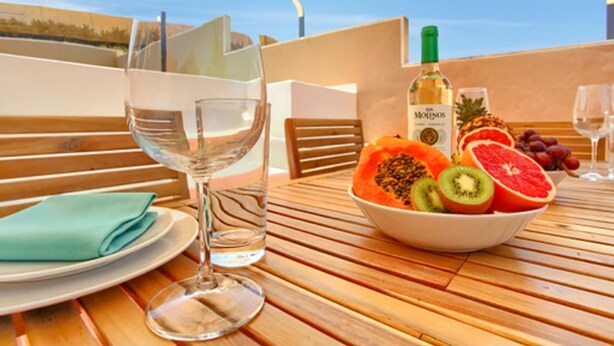 A wooden table with a bowl of fruit, a bottle of wine, and a glass of water.