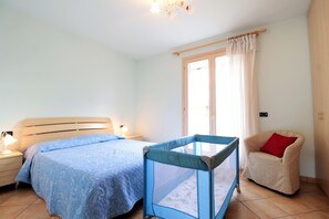 Een slaapkamer met een bed, nachtkastje, stoel, kinderpoort en raam met gordijnen.