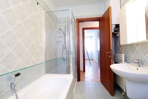 Een badkamer met een douche met glazen wand, een bad en een wastafel.