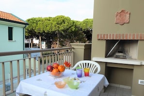 A balcony with a table set for a meal, a grill, and a view of trees.