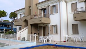 A multi-story residential building with balconies, a swimming pool, and outdoor seating. - Belvilla by OYO Appartamento ROSSO (Jesolo)