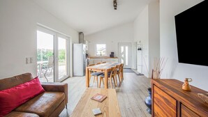 Un salon moderne avec une table à manger en bois, un canapé marron agrémenté d’un coussin rouge et un meuble en bois surmonté d’un vase.