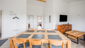 Une pièce spacieuse comprenant une grande table à manger en bois, plusieurs chaises, un téléviseur et un buffet en bois.