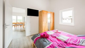 Une chambre à coucher avec un lit, un téléviseur fixé au mur, une armoire en bois et une fenêtre.