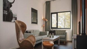 Un salon moderne avec un fauteuil en cuir, un canapé gris, une table basse en bois et une cheminée.