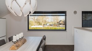 Un espace de salle à manger moderne, doté d’une grande fenêtre, d’une table en bois et d’un luminaire sphérique original.