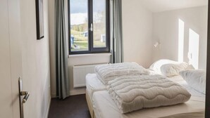 Une chambre d’hôtel avec un grand lit, une fenêtre avec des rideaux, un radiateur et une porte dotée d’une poignée.