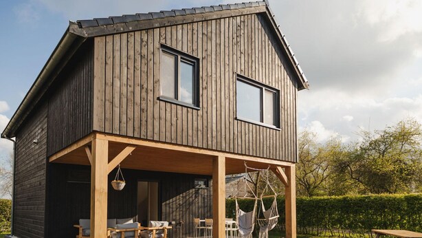 Une maison en bois à deux étages, dotée d’un patio couvert.