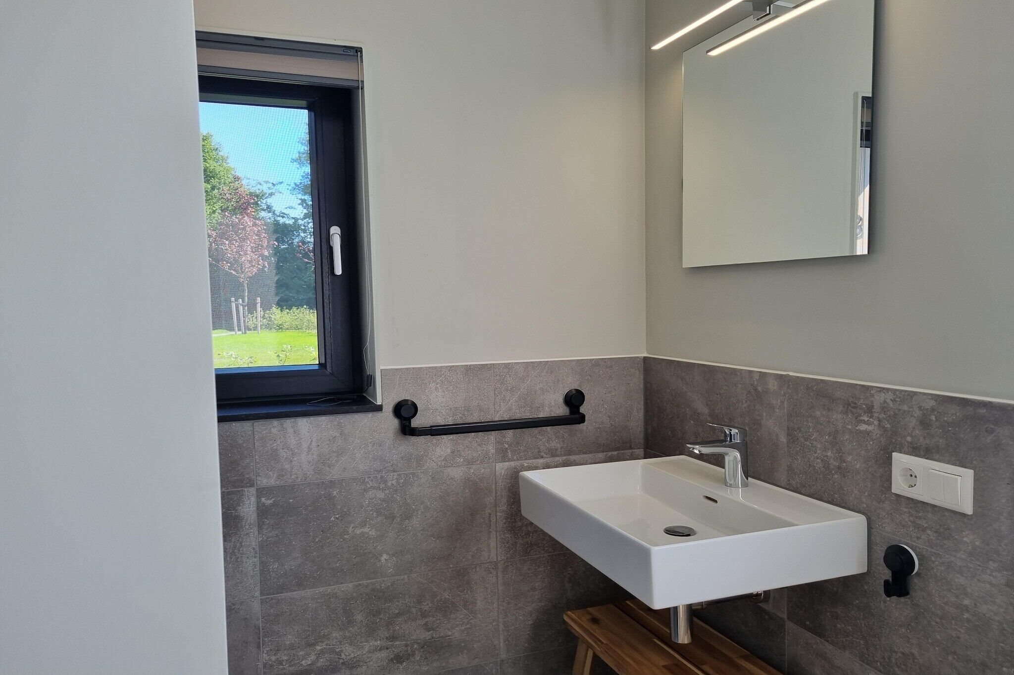 A modern bathroom with a white sink, a mirror, and a window.