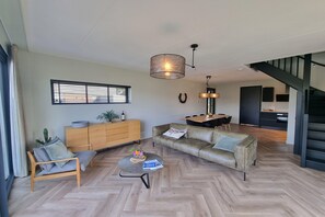 A modern living room with a sofa, a wooden cabinet, a dining area, and a staircase.