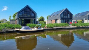 A modern building with a boat docked in front, a canal, and greenery. - Water Villa in Balk by Slotermeer Lake (Balk)