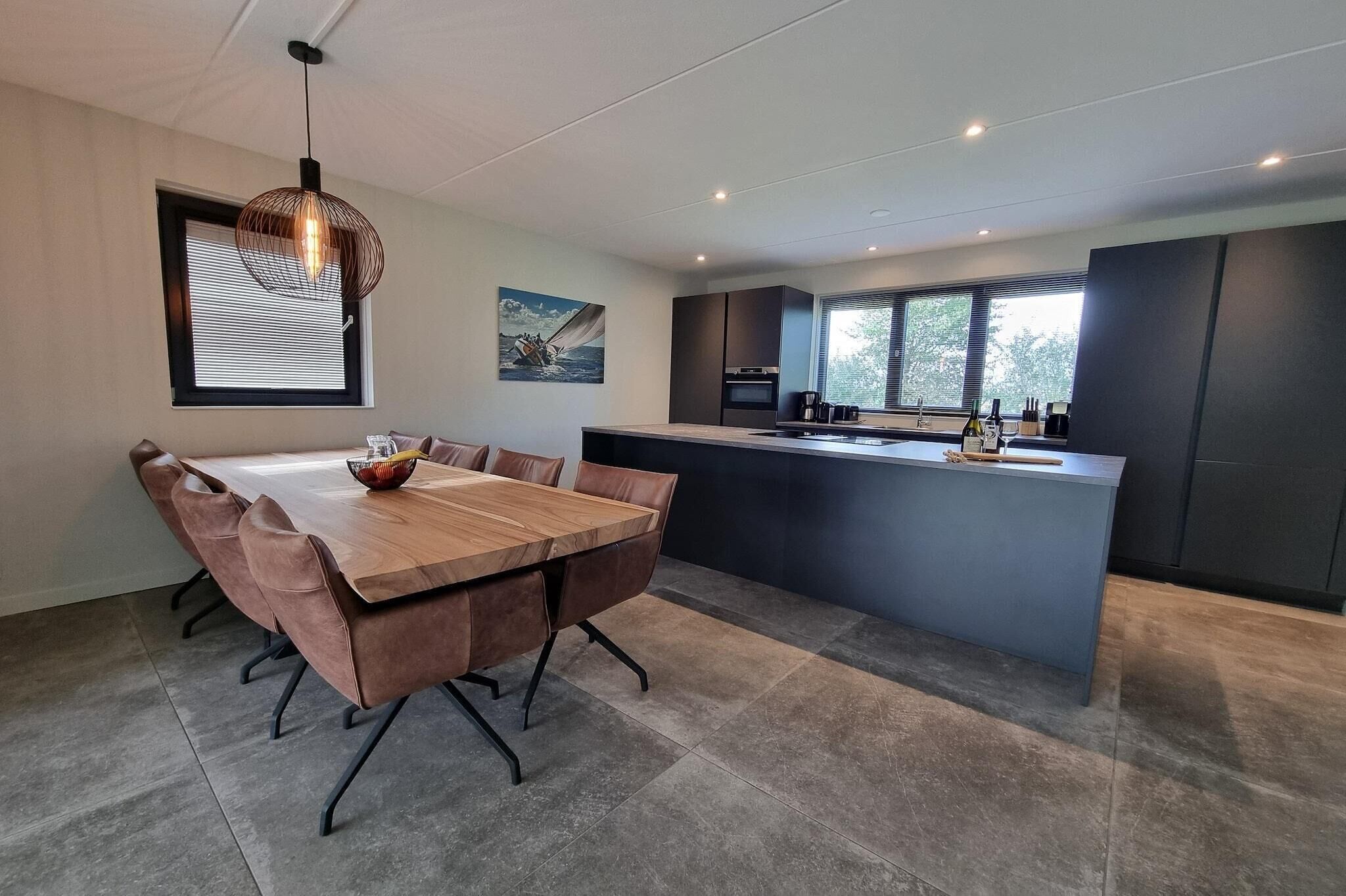 A modern kitchen with a central island, a dining area with a wooden table and chairs, and a large window providing natural light.