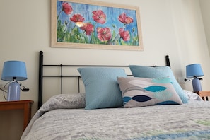 A neatly made bed with a patterned bedspread, two matching pillows, and a framed painting of flowers on the wall.
