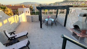 Een terras op het dak met lounge fauteuils, een tafel en een steenoven.