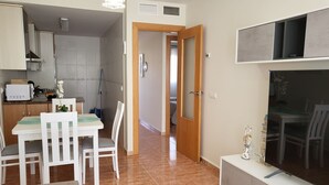 Een compacte woonruimte met een eethoek, een kitchenette en een televisie op een standaard.
