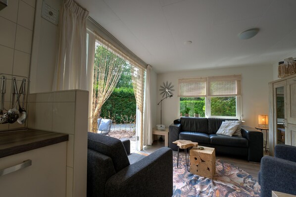 A modern living room with a black leather sofa, a coffee table, and a large window with curtains.