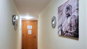 Ein Flur mit einer Holztür am Ende, einem Wandventilator und einer Buddha-Statue.