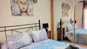 Ein Schlafzimmer mit Bett, Kissen, Nachttisch mit Lampe und Spiegel.