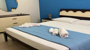 A neatly made bed with a blue bedspread and white linens, a bedside table with a lamp, and a wall-mounted mirror. - Stylish Apartment by the Sea (Ispica)
