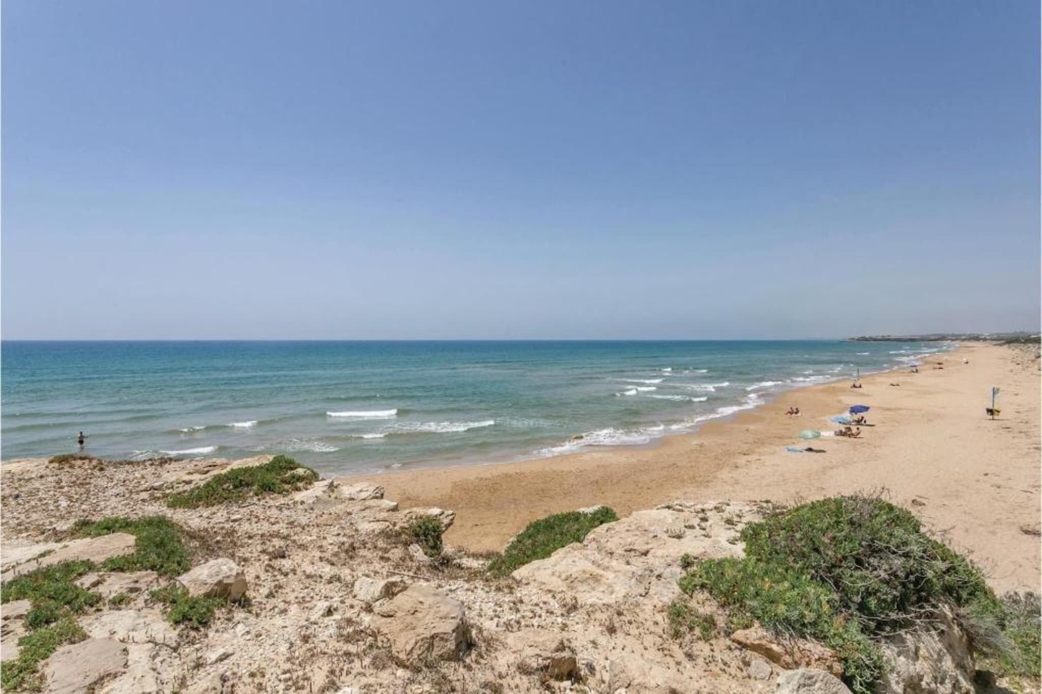 Ein Strand mit blauem Himmel, ruhigem Wasser und wenig Vegetation.