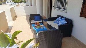 A balcony with wicker furniture, a table with a fruit platter, and a view of the street. - Stylish Apartment by the Sea (Ispica)