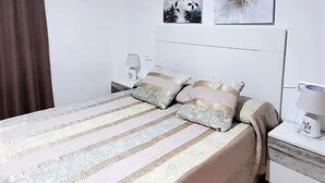 Een keurig opgemaakt slaapkamer met een bed, twee nachtkastjes en een bijzetmeubel.