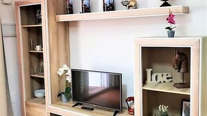 Een houten tv-meubel met een flatscreen televisie, planken met decoratieve objecten, en een plank met een 'Love'-bordje.