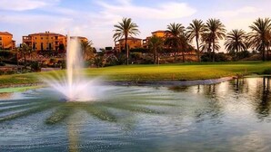 Una fuente en una zona ajardinada con palmeras y edificios al fondo.