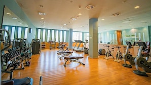 Un gimnasio amplio con diversos equipos de ejercicio, ventanas grandes y suelo de madera.