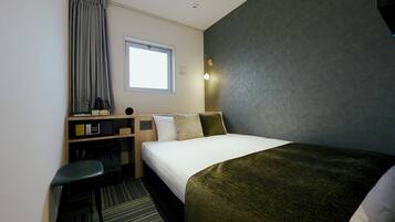 A hotel room with a bed, a desk, a chair, a window, and a wall-mounted light.