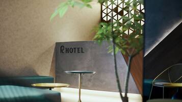 Interior de un hotel con un letrero que dice 'HOTEL', un sofá verde, una mesita redonda y una planta en maceta.