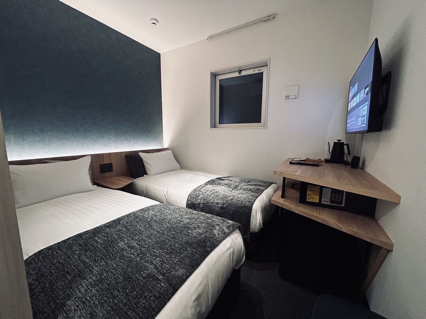 Una habitación de hotel con dos camas, televisión, escritorio con cafetera y ventana.
