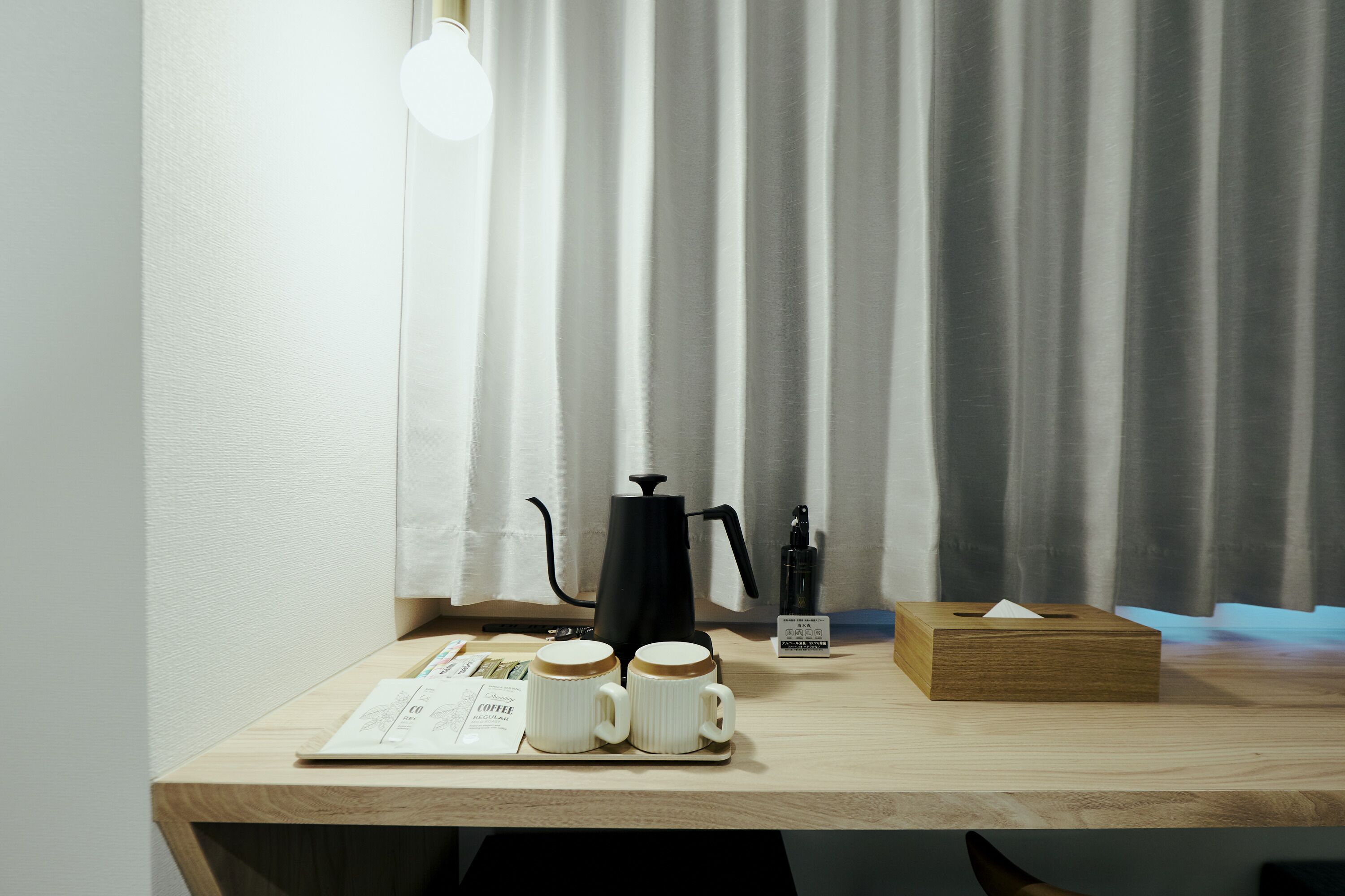 A wooden table with a coffee maker, two white mugs, a tissue box, and a menu.