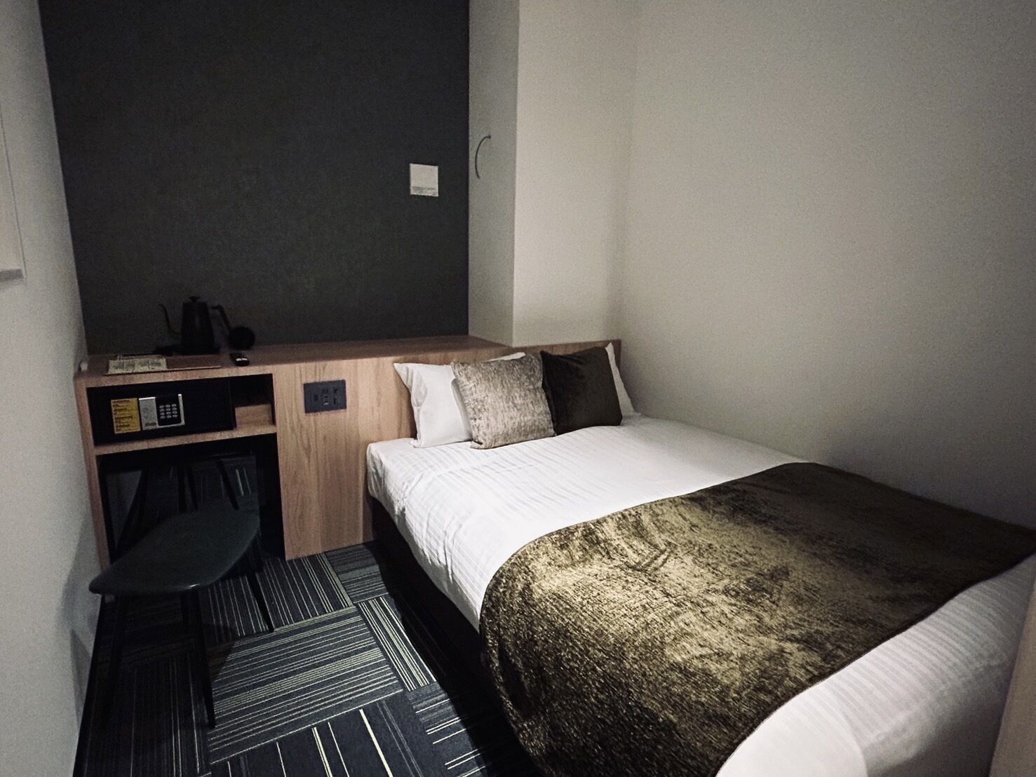 Una habitación de hotel pequeña con una cama individual, un escritorio pequeño con una silla y un microondas.