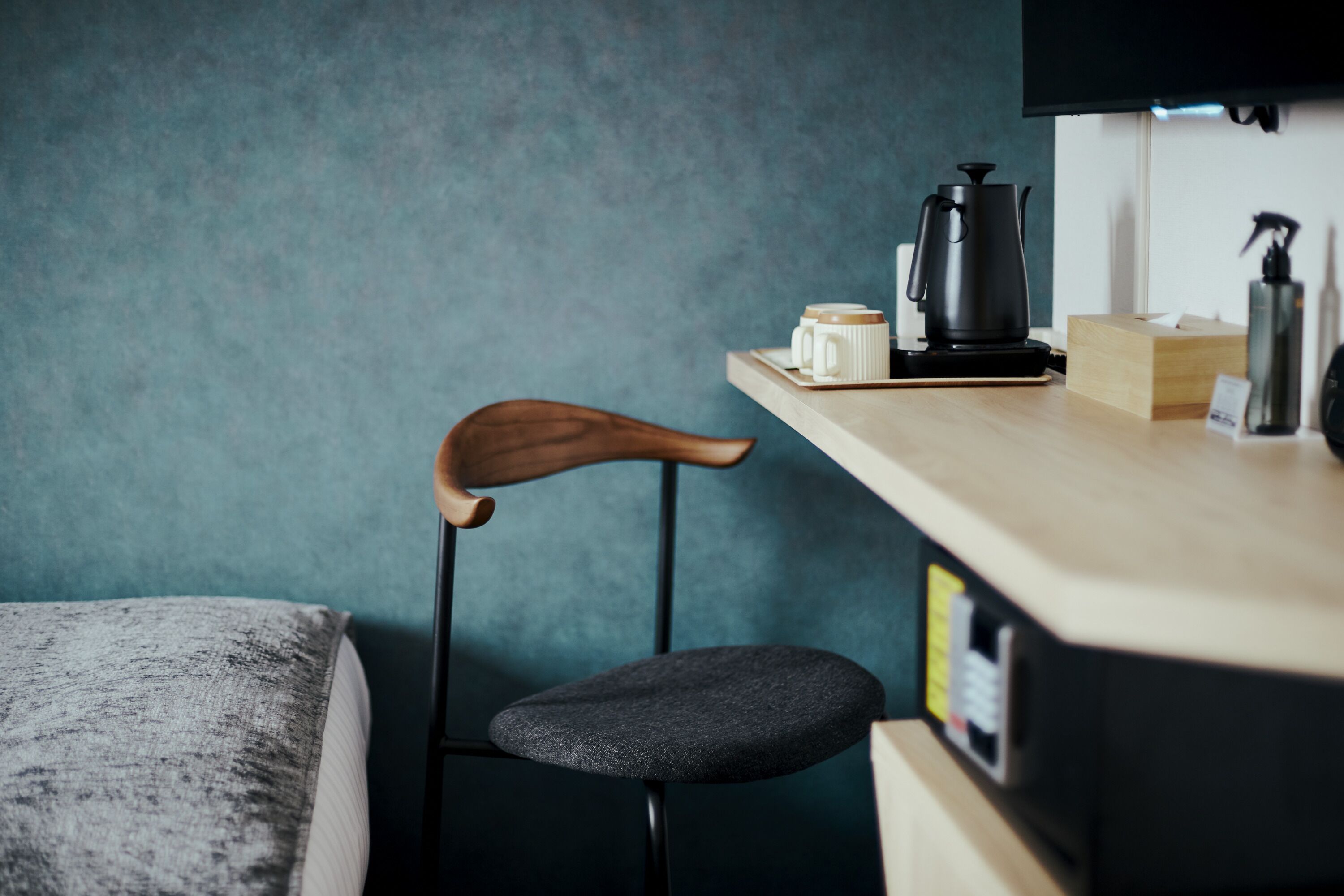 Una kitchenette moderna y pequeña con una silla de madera, un taburete negro, una cafetera y una caja de pañuelos sobre una encimera de tonos claros.