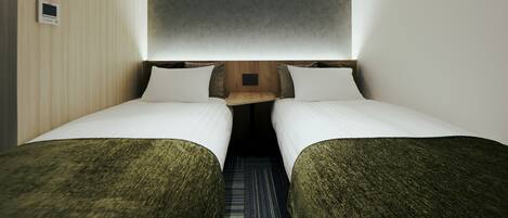 A compact room with two single beds, a small wooden table, and a wall-mounted air conditioner.