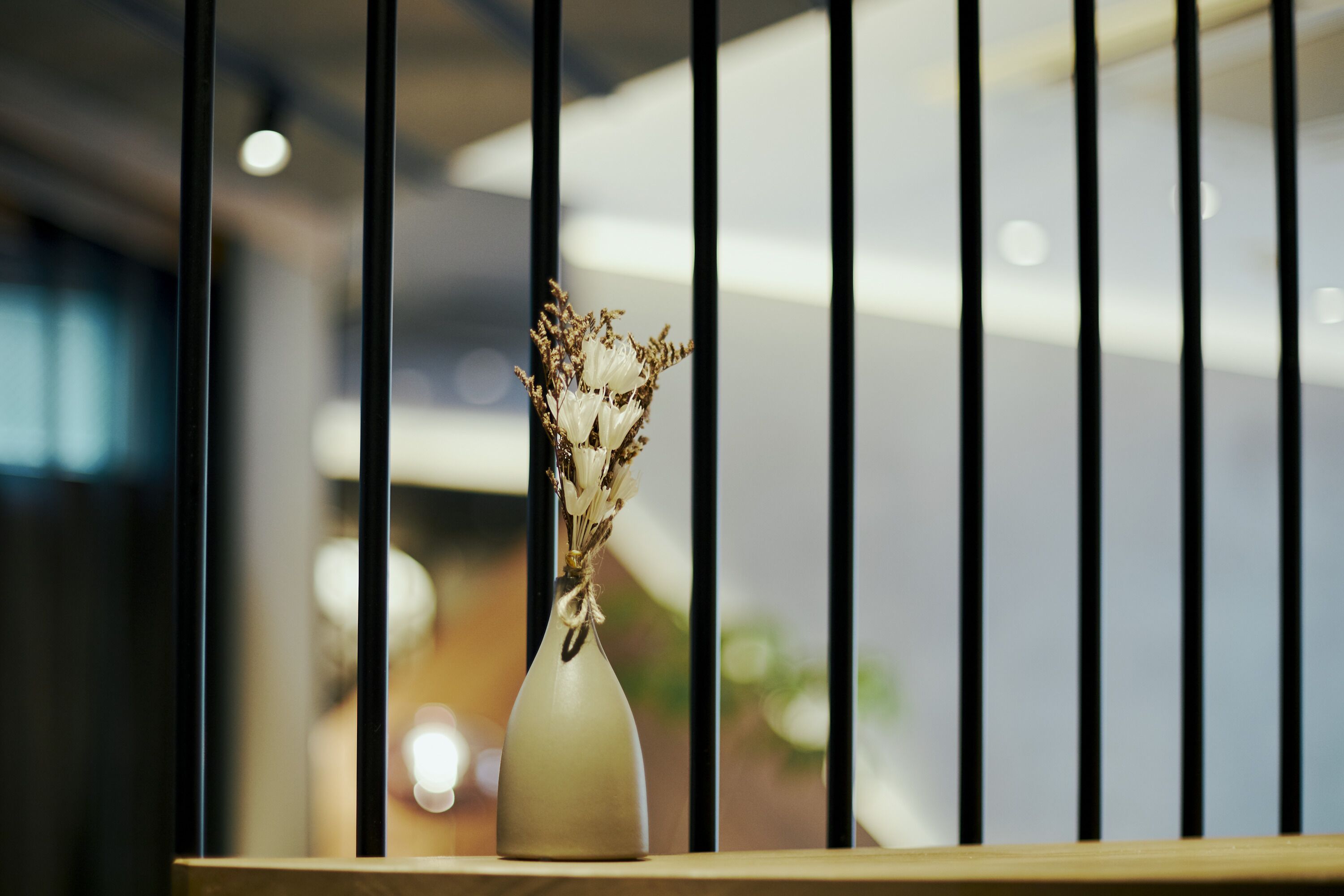 A vase with dried flowers on a wooden ledge, with a blurred indoor background.