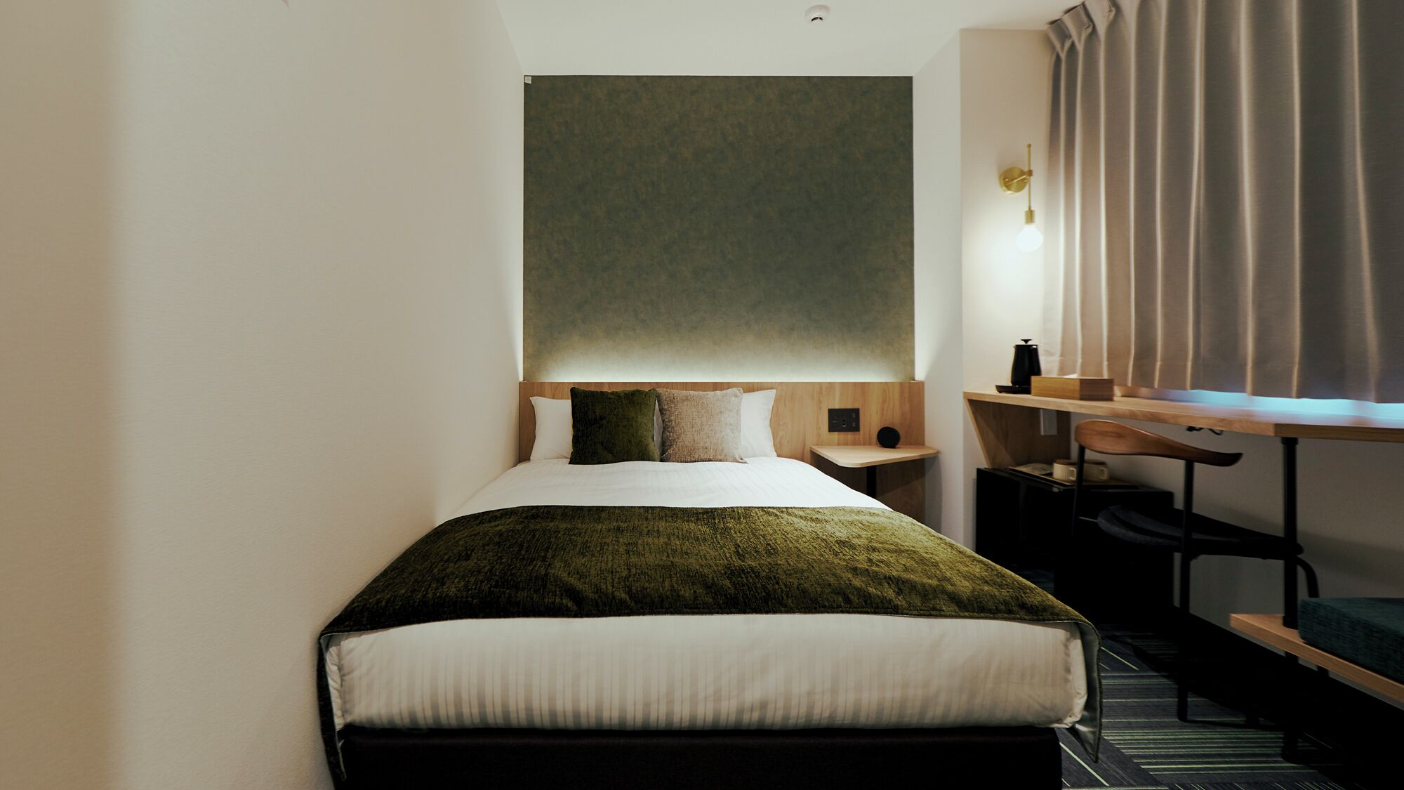 A hotel room with a bed, a desk, a chair, and a window with curtains.