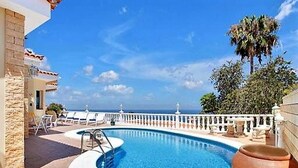 A pool with a clear view of the ocean, a white fence, and a palm tree.