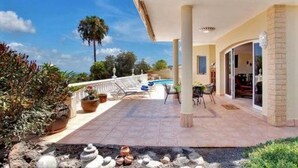 A covered outdoor area with a pool, seating, and potted plants.