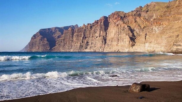 A beach with a rocky cliff and waves.