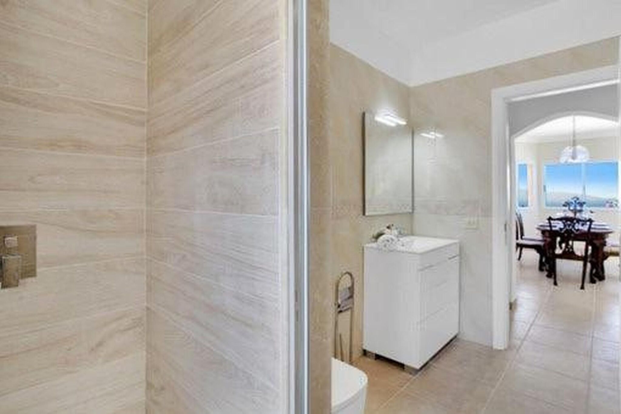 Uma casa de banho moderna com um espelho grande, uma sanita branca e uma área de duche.