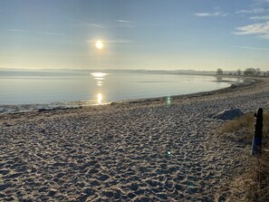 Ein Strand mit Fußspuren, die zum Wasser führen, ein klarer Himmel und ein weiter Horizont.