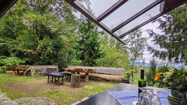 An outdoor seating area with a table, benches, and a view of a forest. - Holiday Home in Edlitz near Ski Slopes (Edlitz)